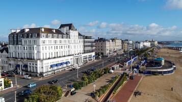 A coastal hotel with multiple floors, a beach promenade, and a view of the sea.