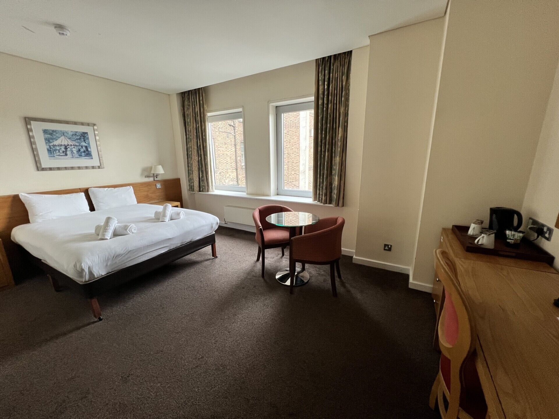 A hotel room with a bed, a small table, a chair, a window, and a picture on the wall.
