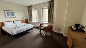 A hotel room with a bed, a small table, a chair, a window, and a picture on the wall.