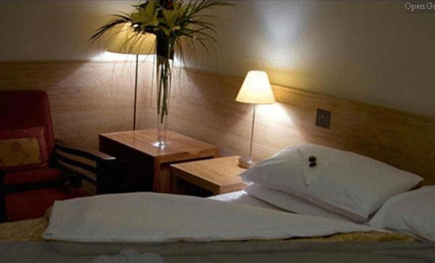A hotel room with a bed, a nightstand, a lamp, and a chair.