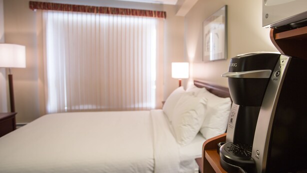Ein Hotelzimmer mit Bett, Kaffeemaschine, Lampe und einem Fenster mit Jalousien.