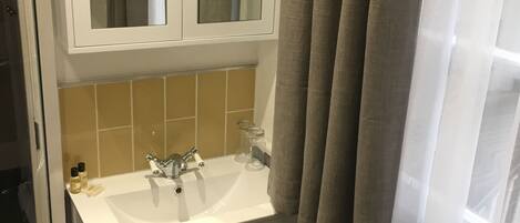 Een badkamer met een witte wasbak, een spiegel erboven en een toiletrolhouder aan de muur.