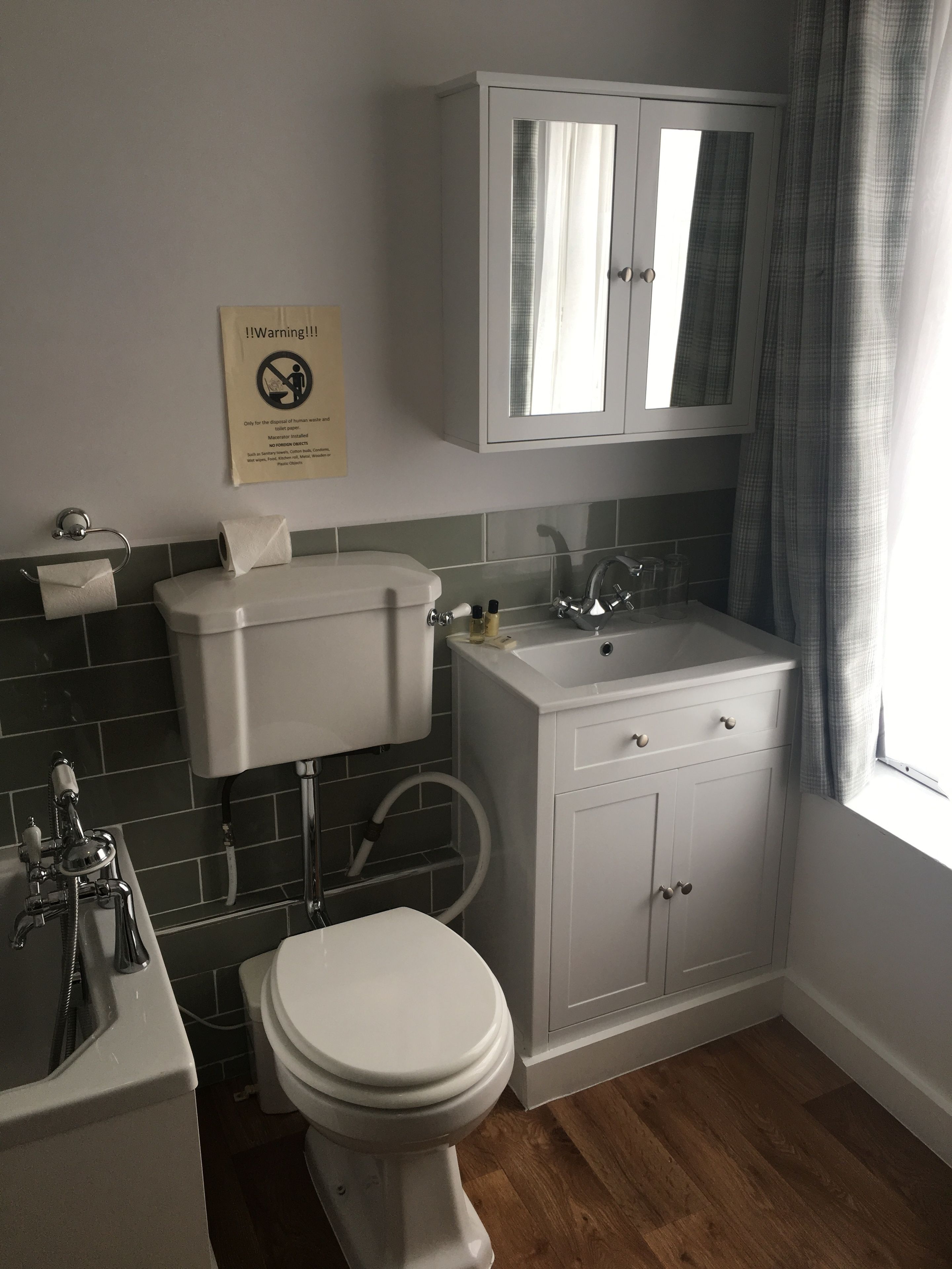 A bathroom with a toilet, sink, and bathtub. There is a warning sign on the wall and a window with curtains.