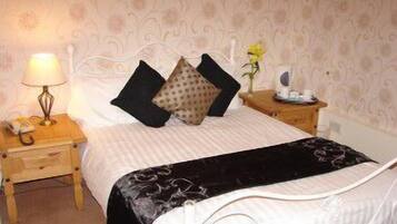 A neatly made bed with a white and black bedspread, two black pillows, and a wooden nightstand with a lamp.