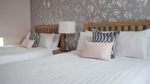 A hotel room with two beds, each with white bedding and patterned pillows. There is a nightstand with a lamp between the beds. The walls have a floral wallpaper design. - The Star Hotel (Southampton)