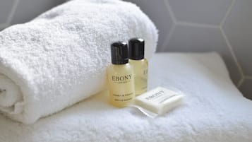 Una toalla blanca doblada con cuidado, dos botellas de jabón 'Ebony London Honey & Mango Bath & Shower' y una barra del mismo jabón.