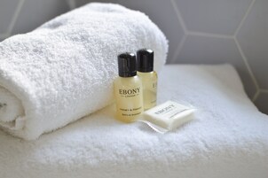 Una toalla blanca doblada con cuidado, dos botellas de jabón 'Ebony London Honey & Mango Bath & Shower' y una barra del mismo jabón.