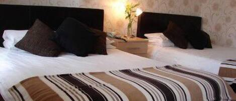 A hotel room with two beds, each with a striped bedspread, a nightstand with a lamp, and a floral wallpaper pattern.