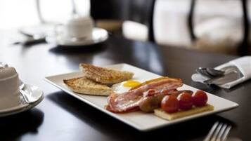 A breakfast plate with toast, bacon, eggs, and tomatoes on a white plate.