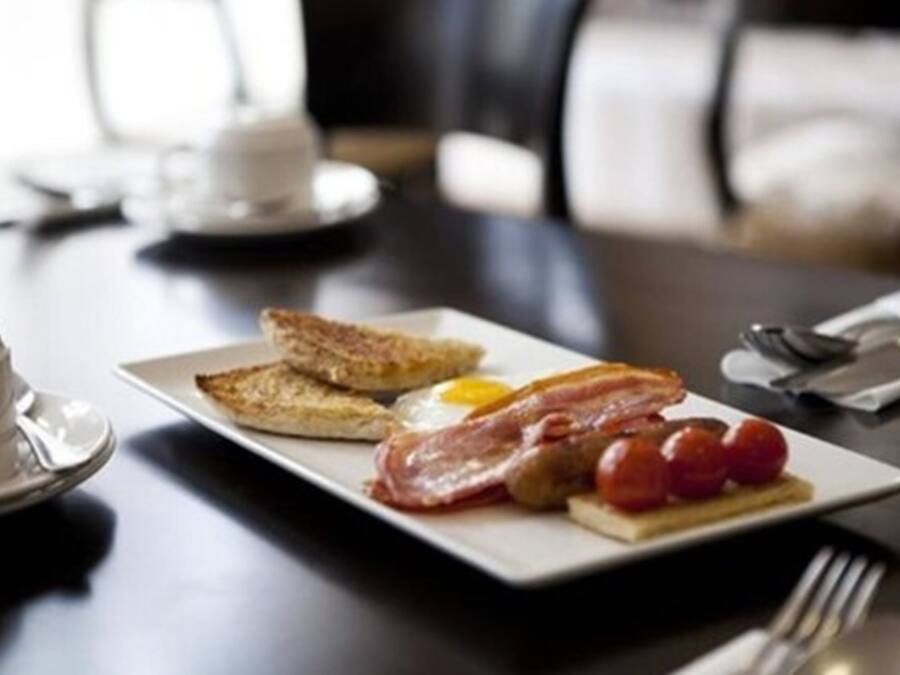 A breakfast plate with toast, bacon, eggs, and tomatoes on a white plate.