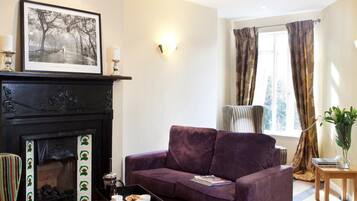 A living room with a fireplace, a purple sofa, a striped armchair, and a small table with a vase.