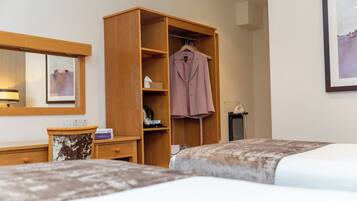 Habitació d'hotel amb armari de fusta, llit amb edredó estampat, tauleta de nit amb làmpada i quadre amb marc a la paret.