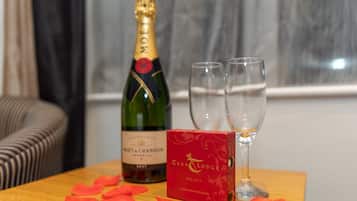 A bottle of Moët & Chandon champagne, two glasses, and a box of Cara & Lodge chocolates on a wooden table.