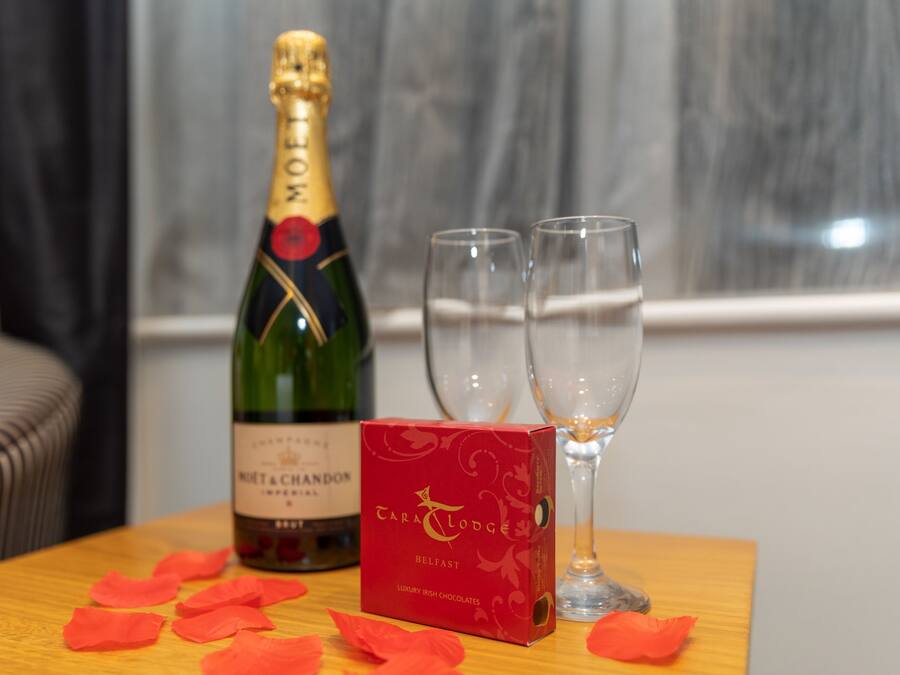 Eine Flasche Moët & Chandon Champagner, zwei Gläser und eine Schachtel Cara & Lodge Pralinen auf einem Holztisch.