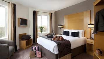 A hotel room with a bed, a chair, a TV, a desk, and a wardrobe.