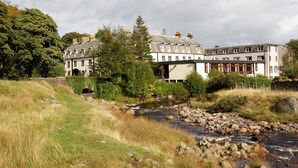 Een hotel aan de rivier met een pad van stenen dat naar de ingang leidt, omringd door weelderige begroeiing en een rustige rivier.