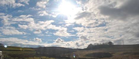 A landscape with a clear sky, scattered clouds, and a bright sun.