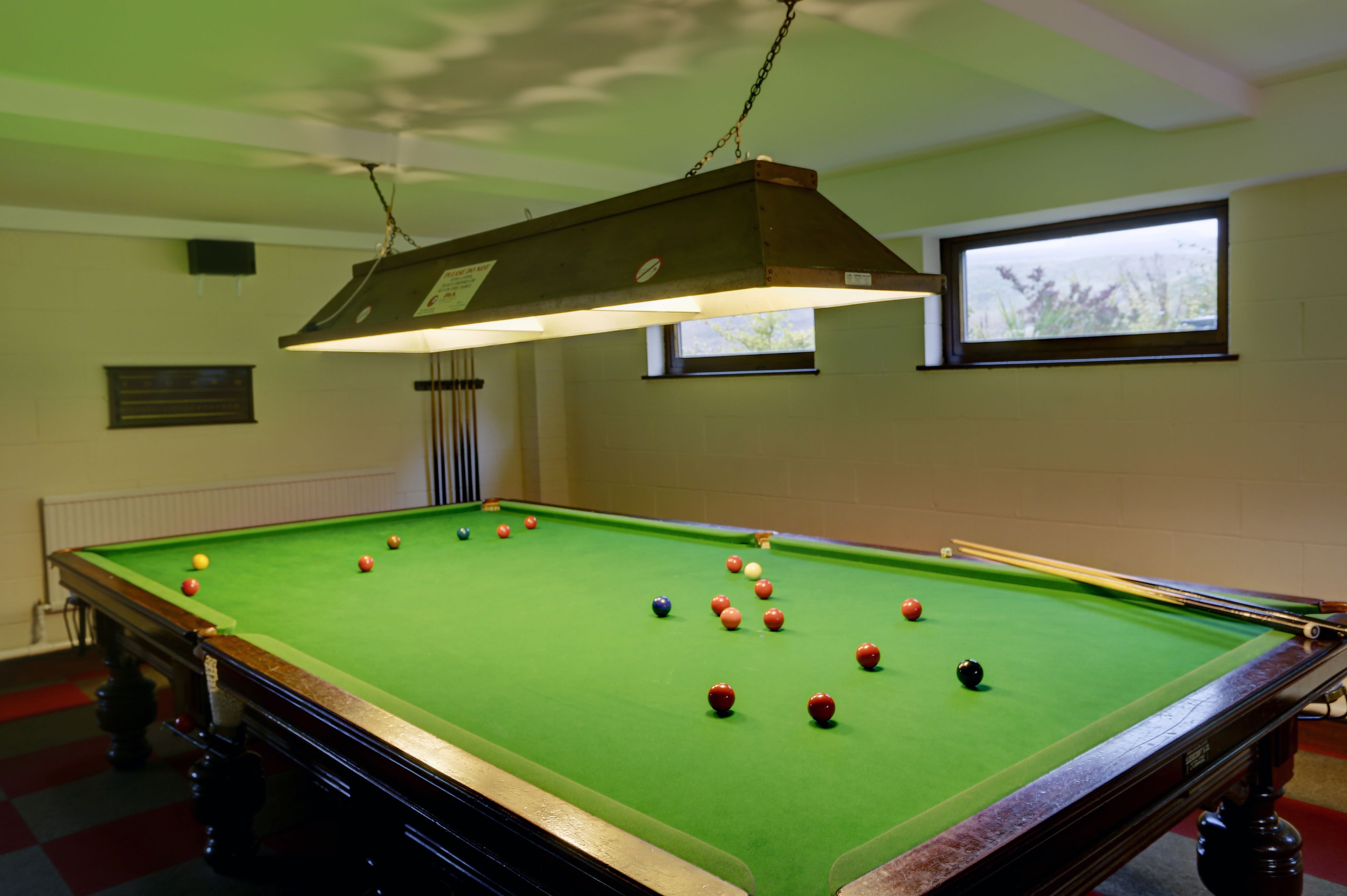 A pool table with balls, a hanging light fixture, and a window with a view.