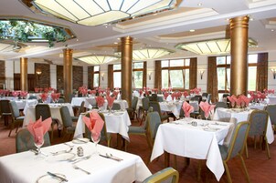 A banquet hall with multiple tables set for dining, featuring gold columns and large windows.