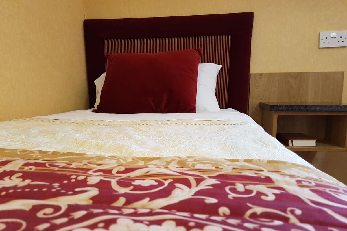 A neatly made bed with a patterned bedspread, a red pillow, and a white pillow.