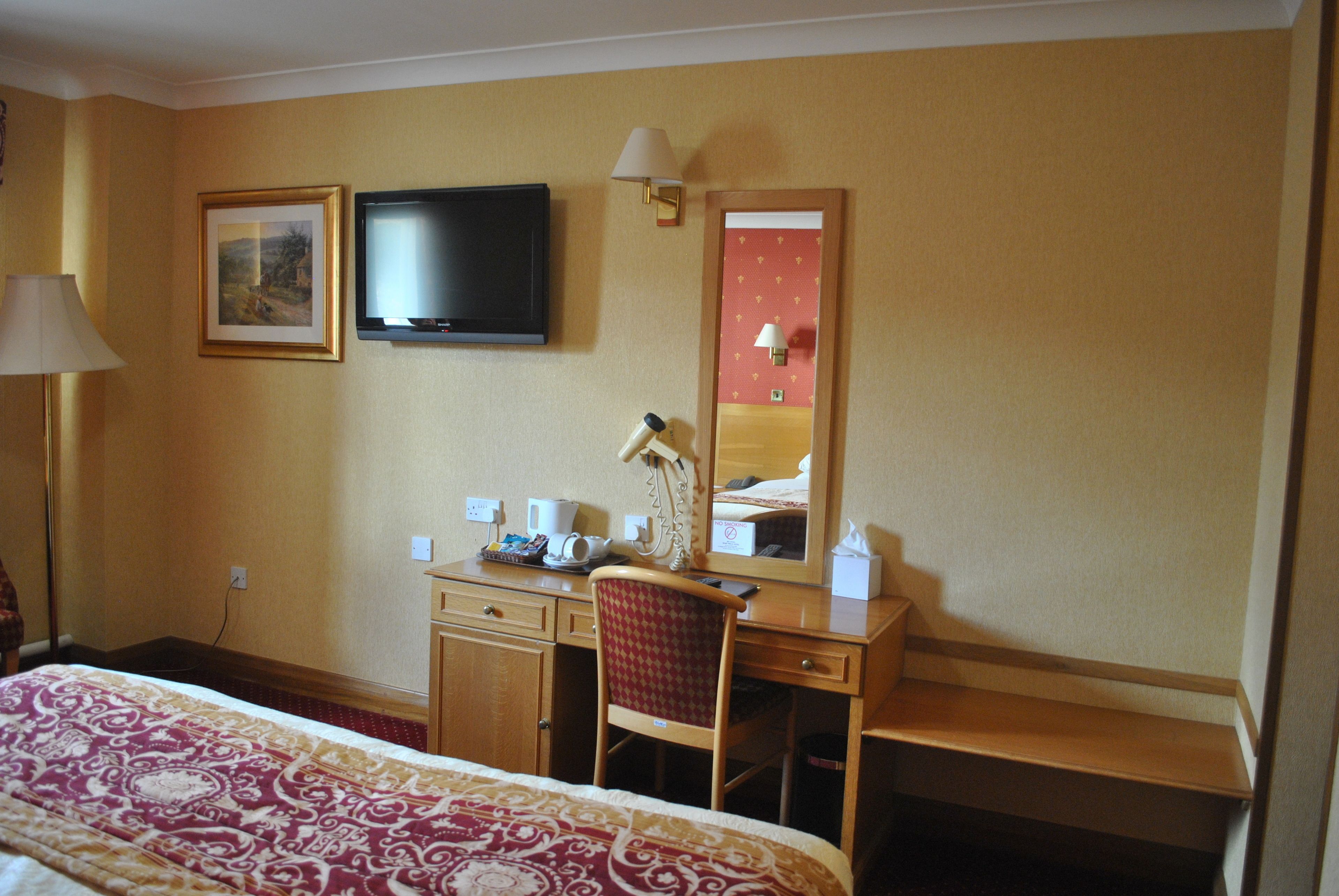 Ein Hotelzimmer mit Bett, Schreibtisch mit Stuhl, Fernseher, Lampe und Spiegel.