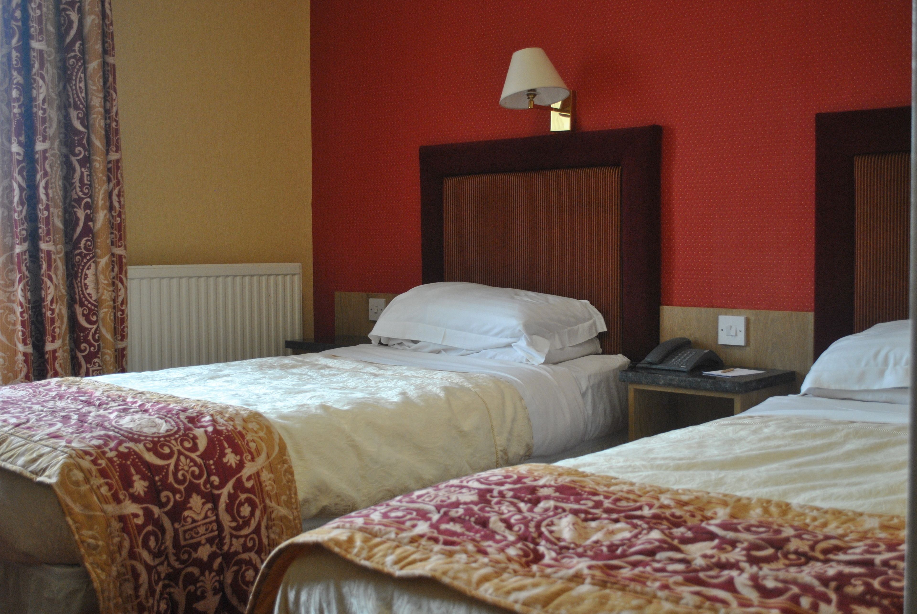 Ett hotellrum med två sängar, en sänglampa, en telefon och ett fönster med gardiner.