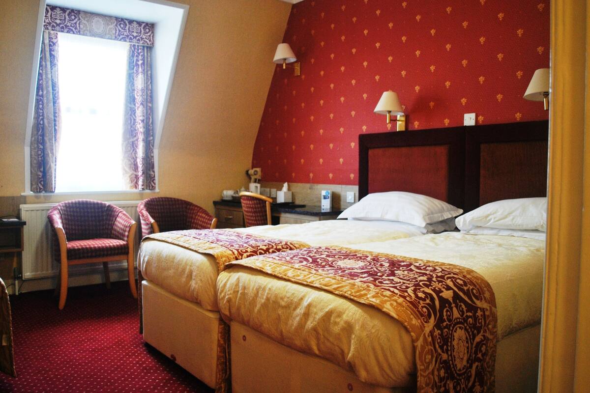 A hotel room with a large bed, two chairs, a nightstand, and a window with curtains.