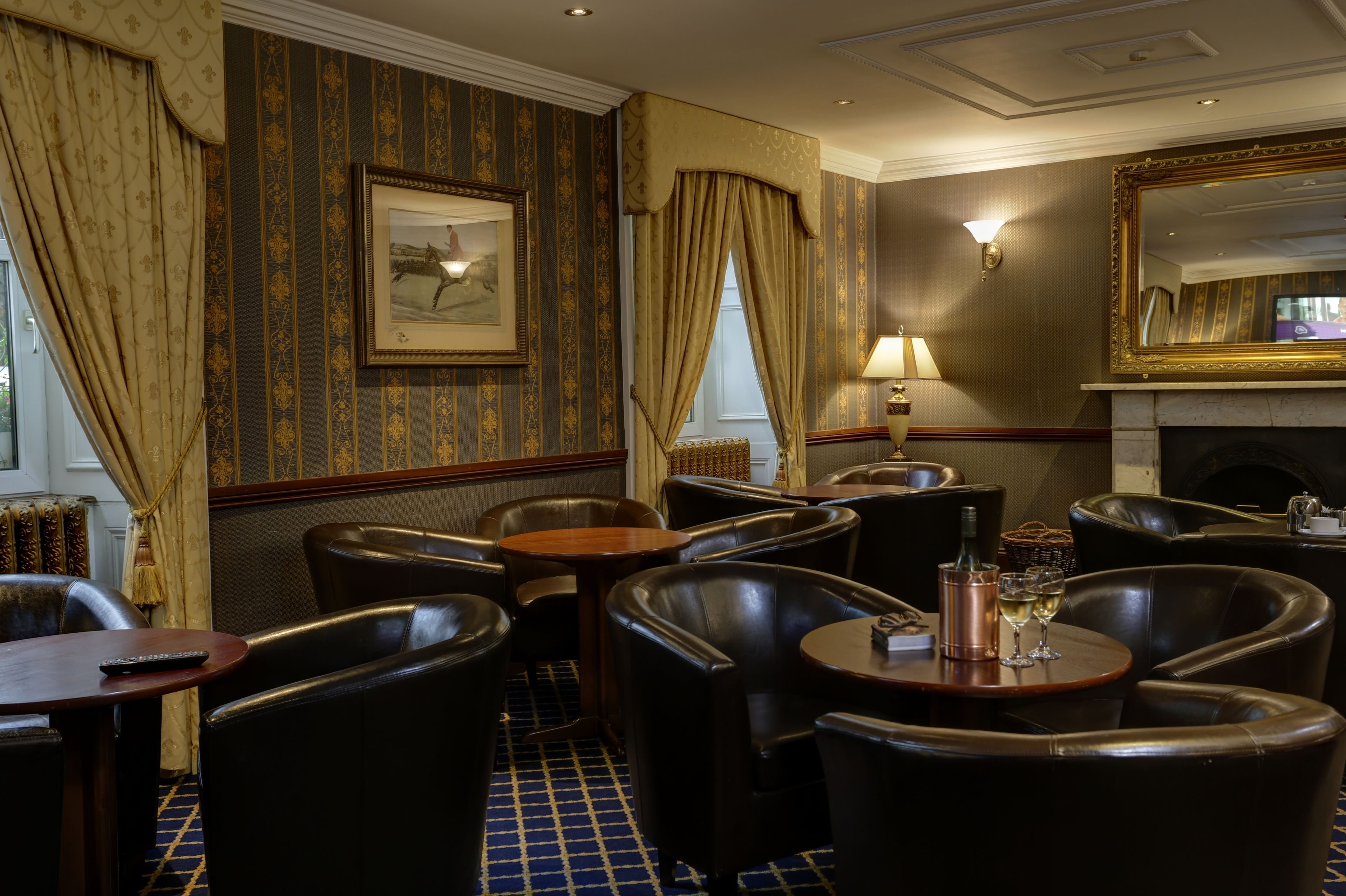 Une chambre d’hôtel avec une cheminée, des fauteuils en cuir, une petite table et un tableau au mur.