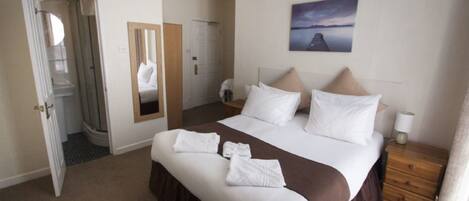 A hotel room with a large bed, a bedside table, a mirror, and a painting on the wall.