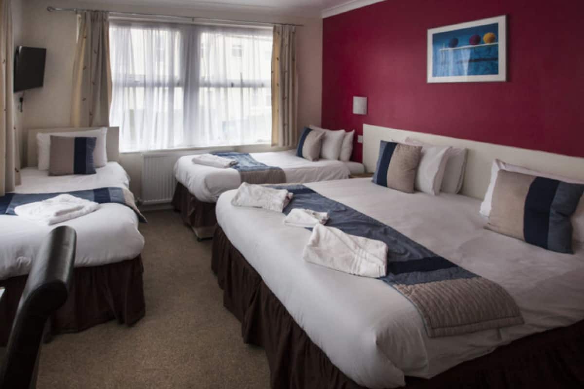 Une chambre d’hôtel avec trois lits, un mur d’accent rouge et une fenêtre avec des rideaux légers.