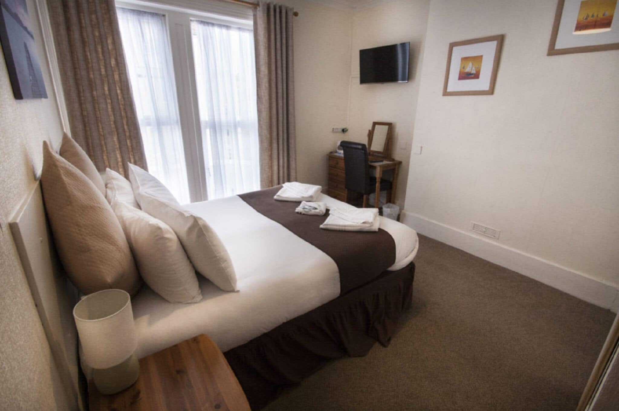 Quarto de hotel com cama, televisão de tela plana, cômoda e janela com cortinas.