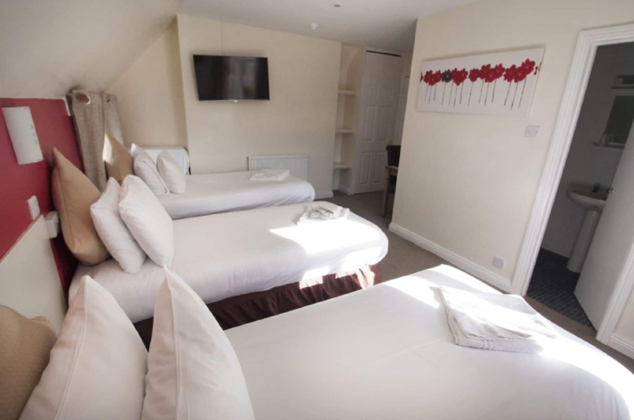 A hotel room with two beds, a TV, a red wall, and a door leading to a bathroom.