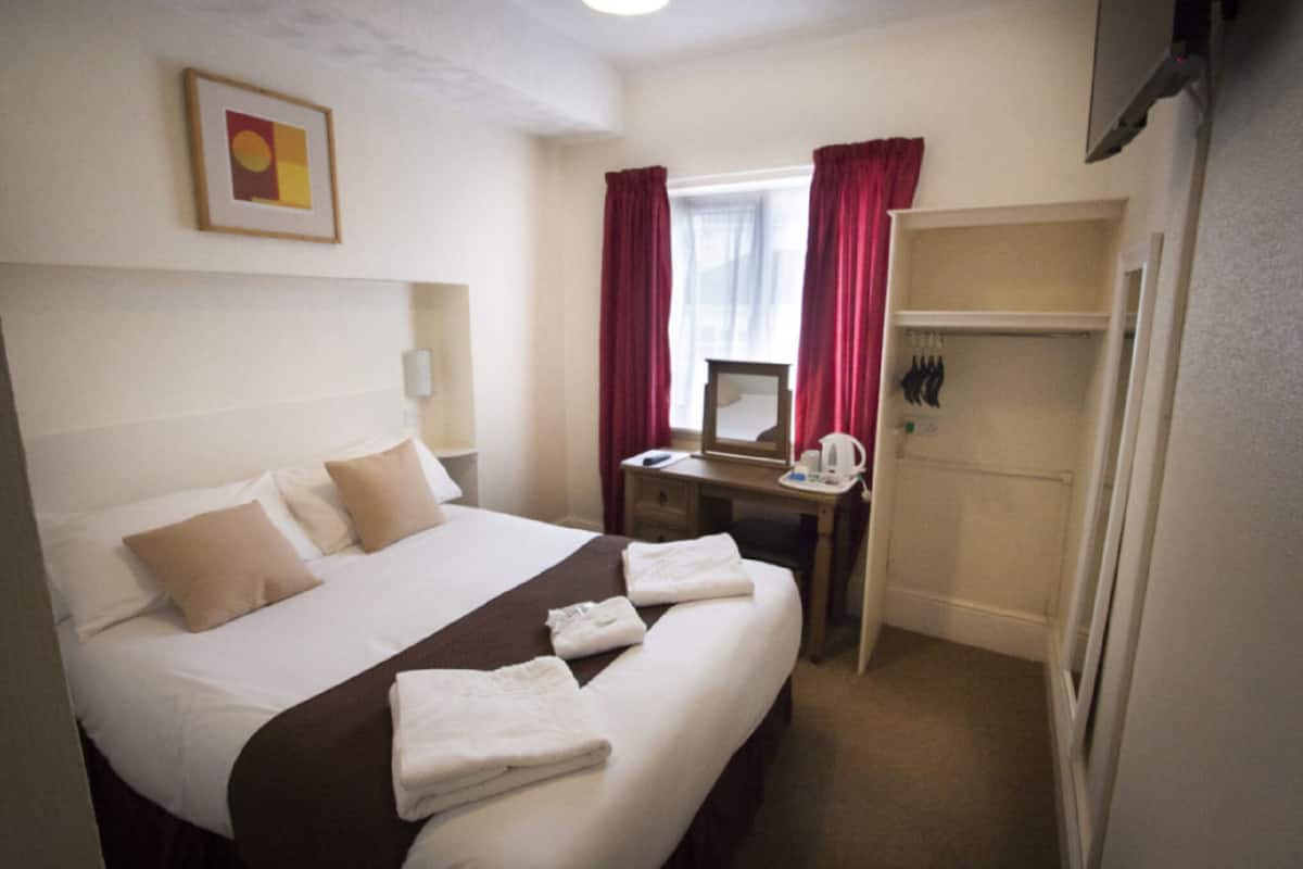 Une chambre d’hôtel comprenant un lit, un bureau, un miroir, une armoire et une fenêtre avec des rideaux.