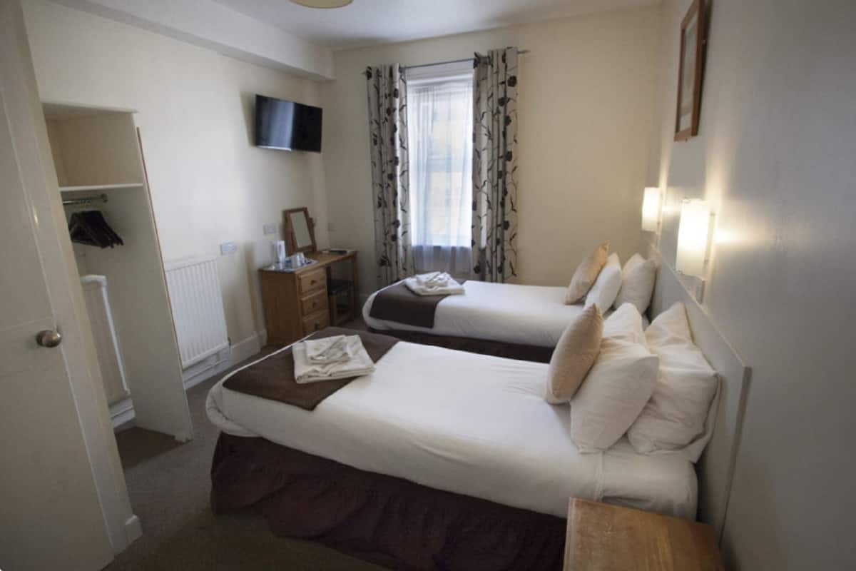 Une chambre d’hôtel avec deux lits, une télévision, une fenêtre avec des rideaux, une table de chevet en bois et une armoire.