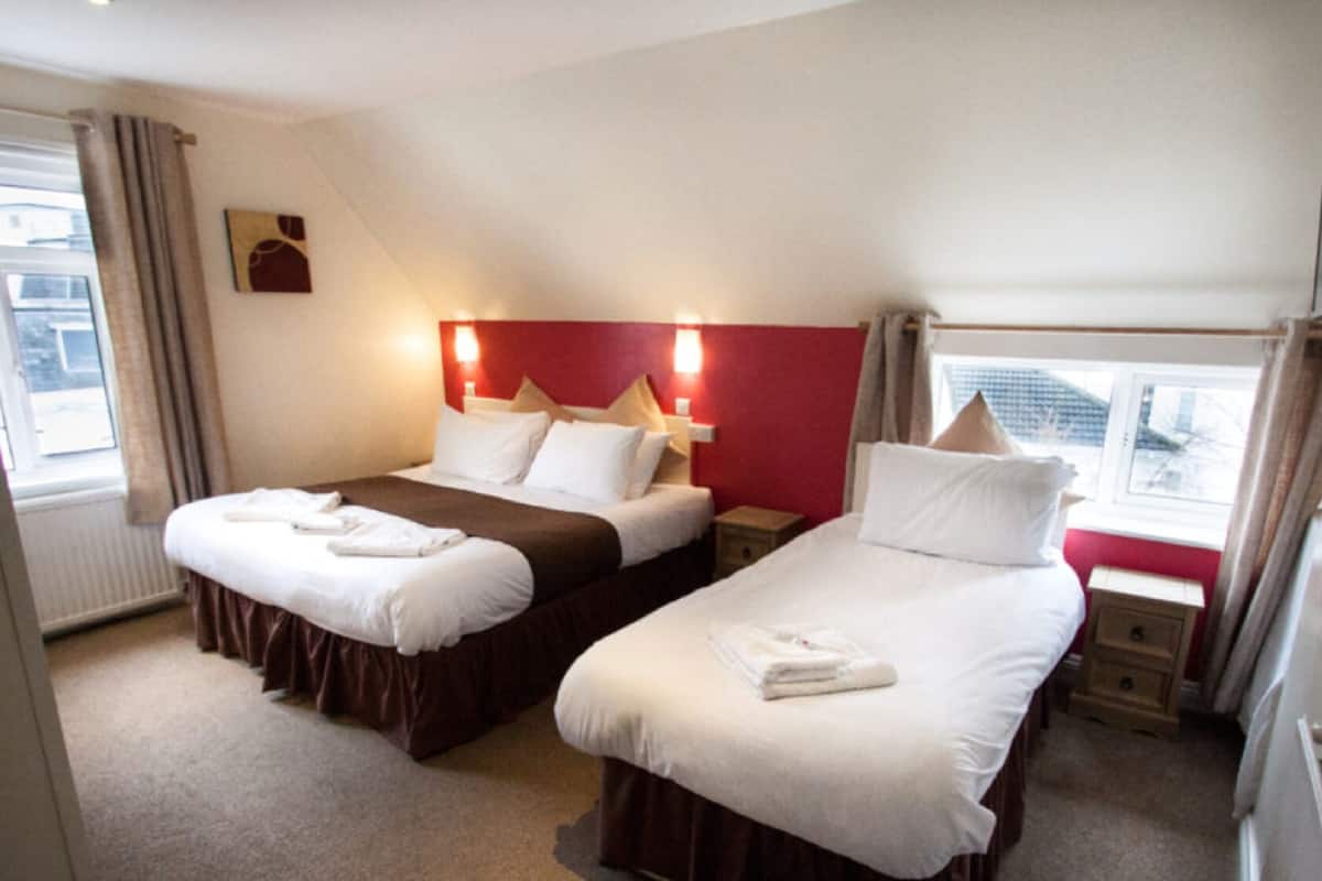 Une chambre d’hôtel avec deux lits, un mur d’accent rouge et une fenêtre avec des rideaux.