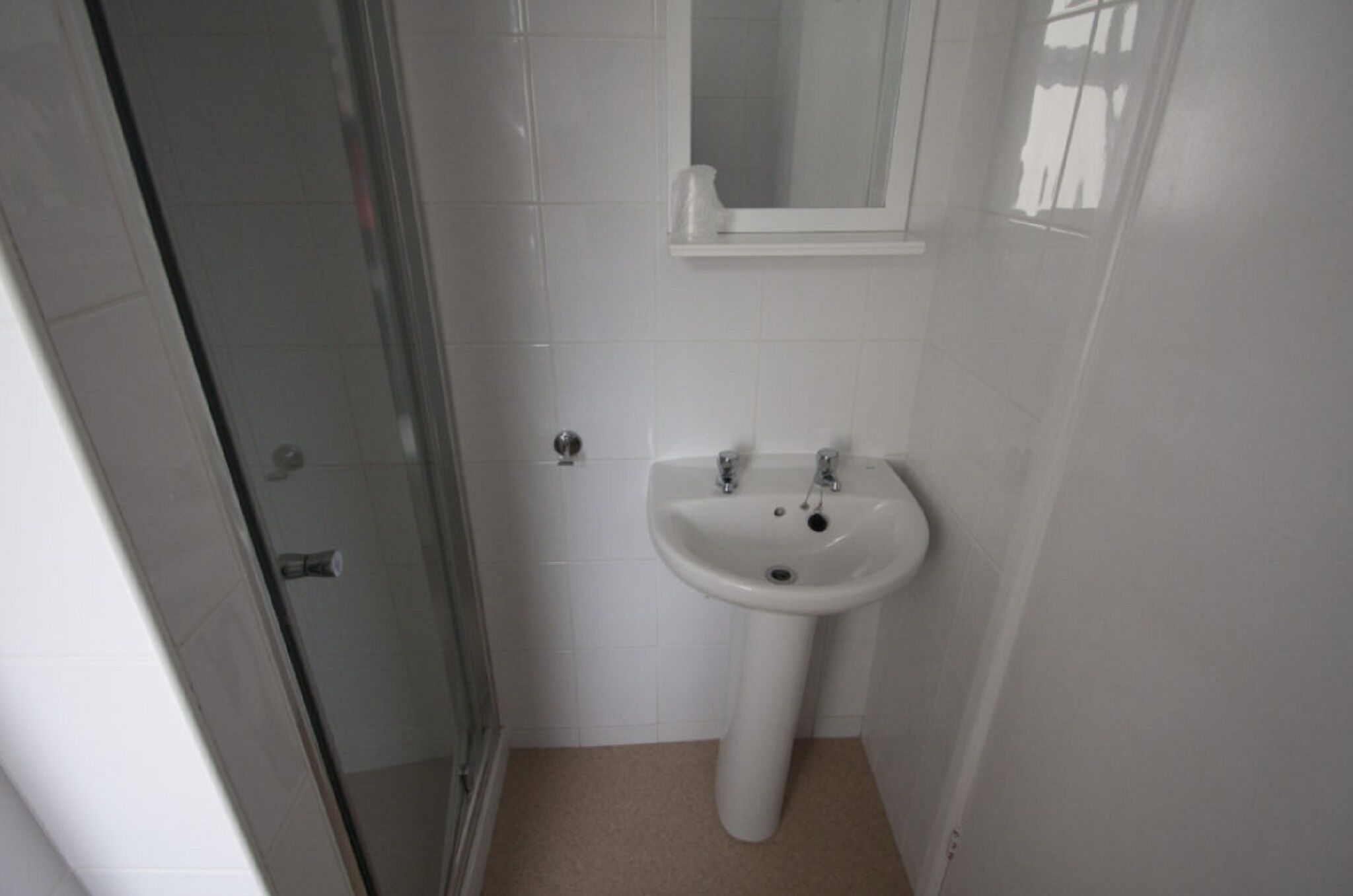Un baño con cabina de ducha de vidrio, un lavamanos pedestal y un espejo sobre él.