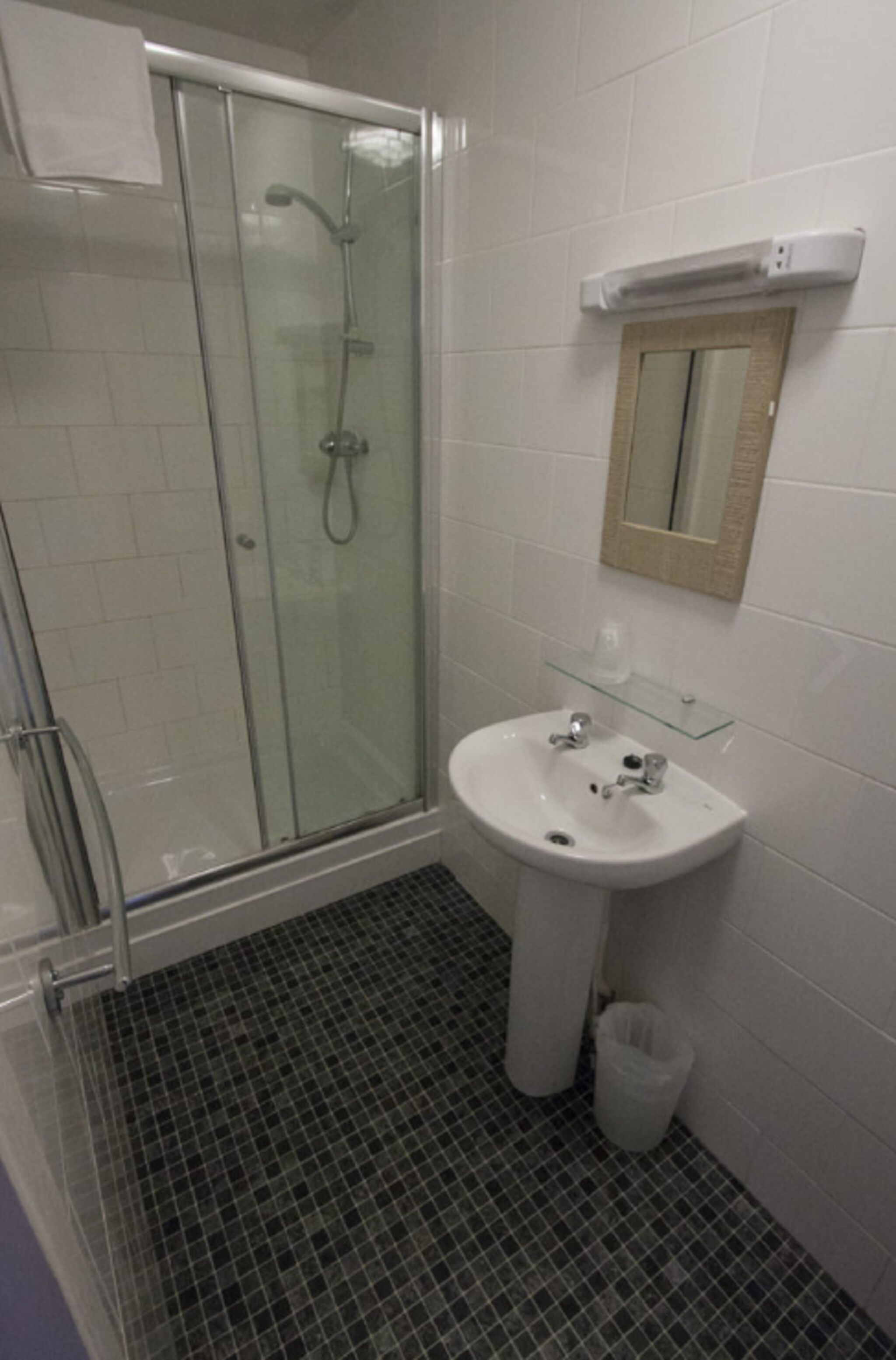 A bathroom with a glass shower enclosure, a white sink, and a mirror above it.