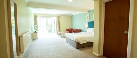 Habitación de hotel con una cama grande, un escritorio y una silla. Tiene una ventana con cortinas y vistas al exterior con vegetación.