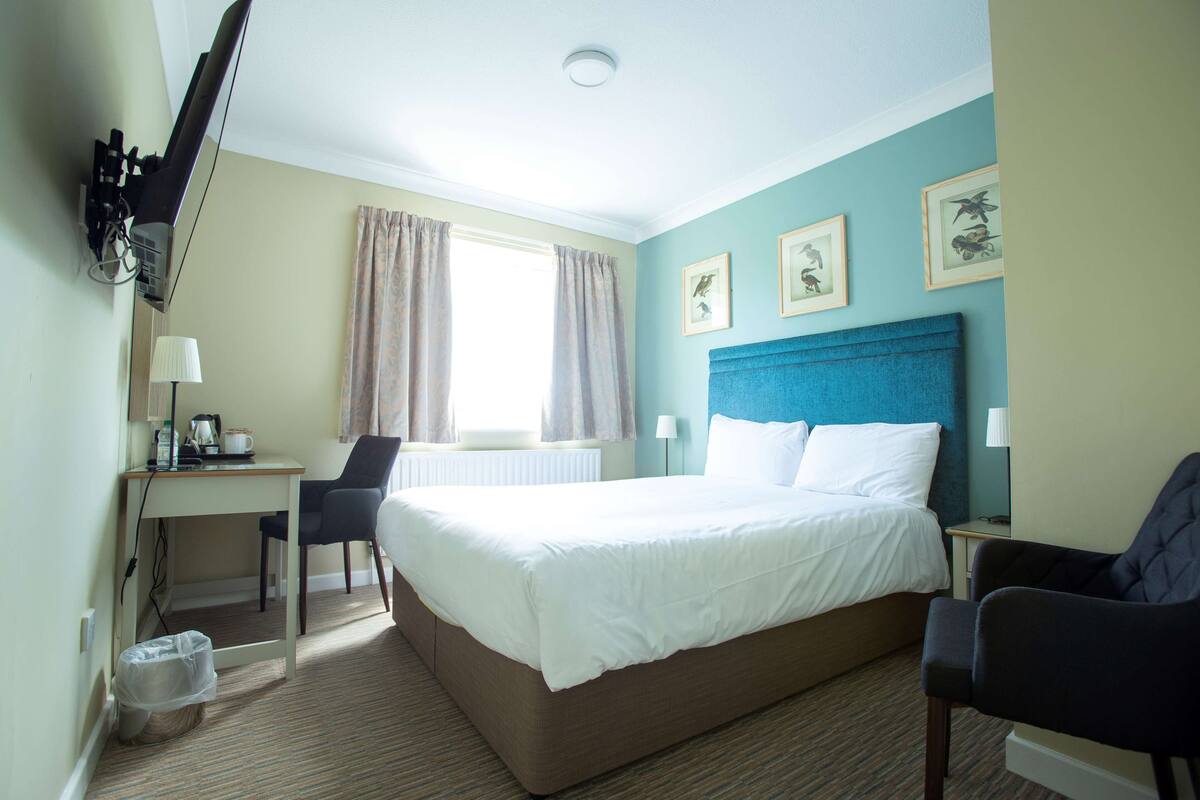 Una habitación de hotel con cama, escritorio, silla y ventana con cortinas.