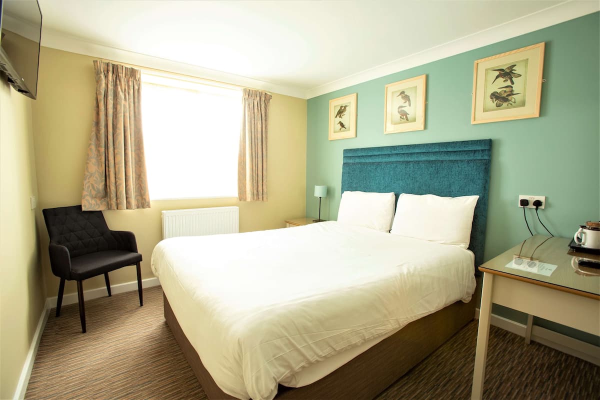 Habitación de hotel con una cama grande, una silla, un escritorio con lámpara y cuadros en la pared.