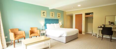 A hotel room with a bed, two armchairs, a desk, and a mirror.