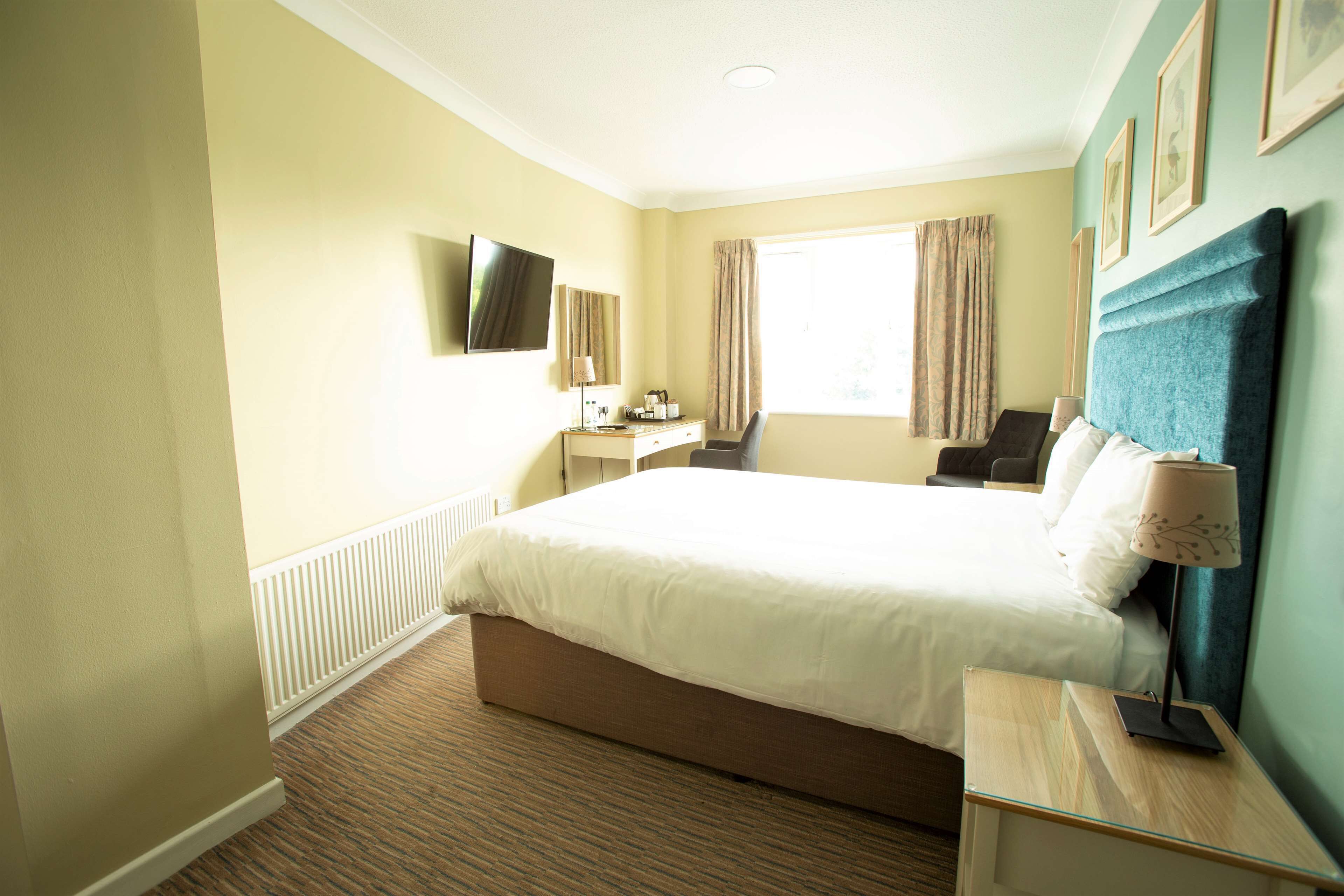 A hotel room with a large bed, a desk, a chair, a TV, and a window with curtains.