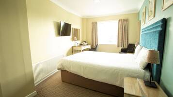 A hotel room with a large bed, a desk, a chair, a TV, and a window with curtains.