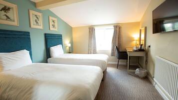 A hotel room with two beds, a desk, a chair, a TV, and framed pictures on the wall.