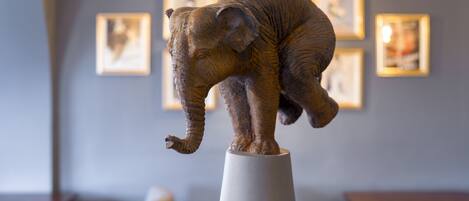 A sculpture of an elephant on a pedestal in a room with framed pictures on the wall.