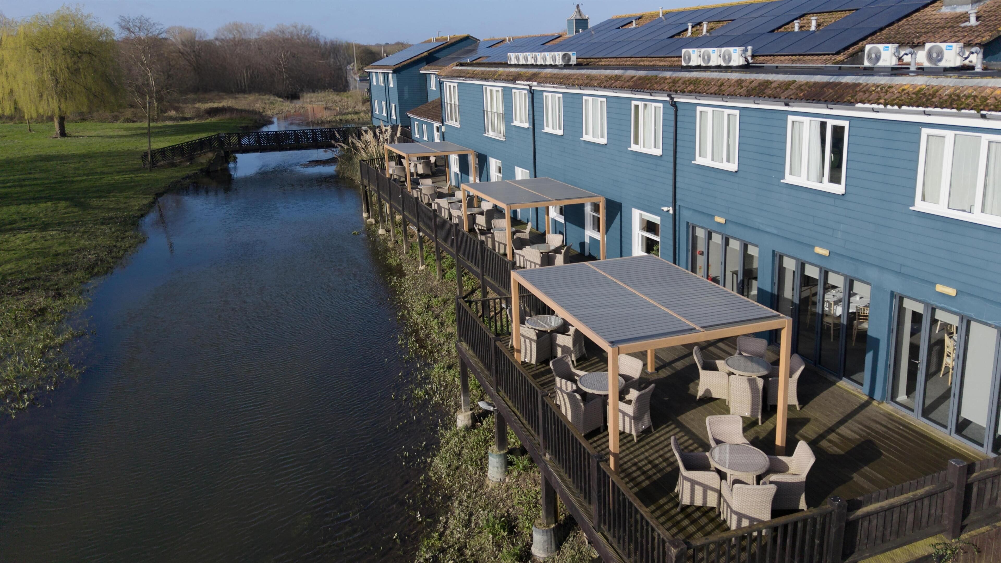 Un hôtel situé au bord de la rivière, doté d’une terrasse, d’un pont et de panneaux solaires sur le toit.