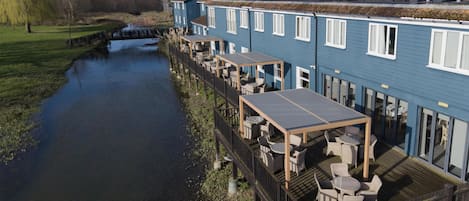 A riverside hotel with outdoor seating, a bridge, and solar panels on the roof.