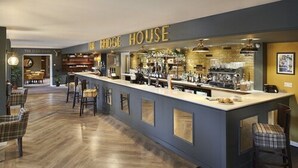 A bar area with a long counter, bar stools, and a sign that reads "THE BRIDGE HOUSE".