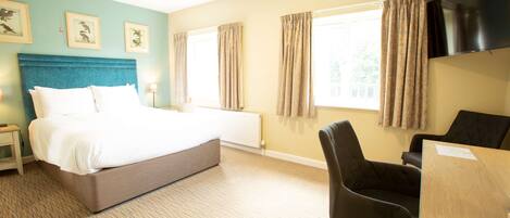 A hotel room with a bed, a desk, a chair, a TV, and a window with curtains.