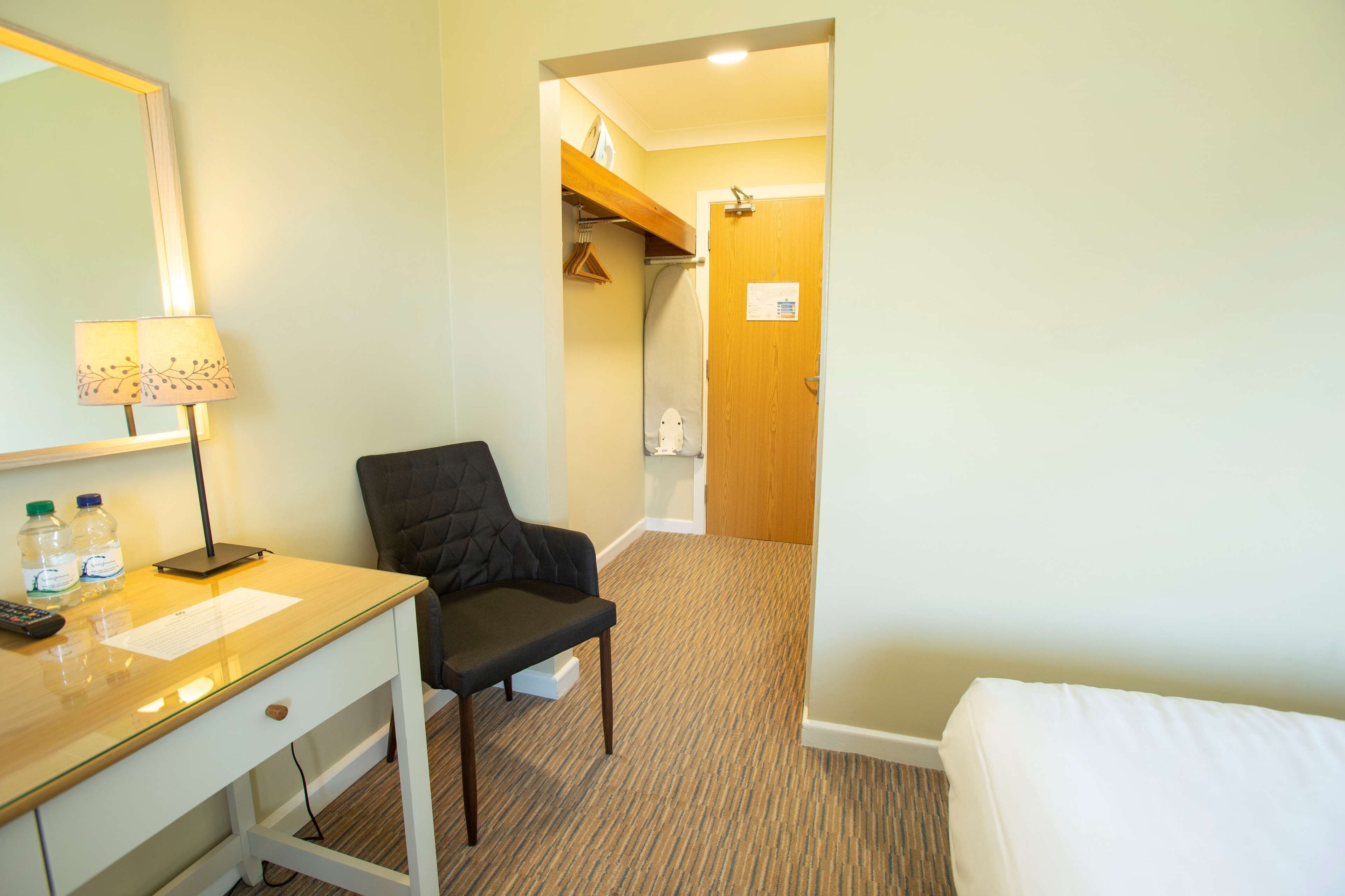 Une chambre d’hôtel équipée d’un bureau, d’une chaise, d’un lit et d’une salle de bain visible à travers une porte ouverte.